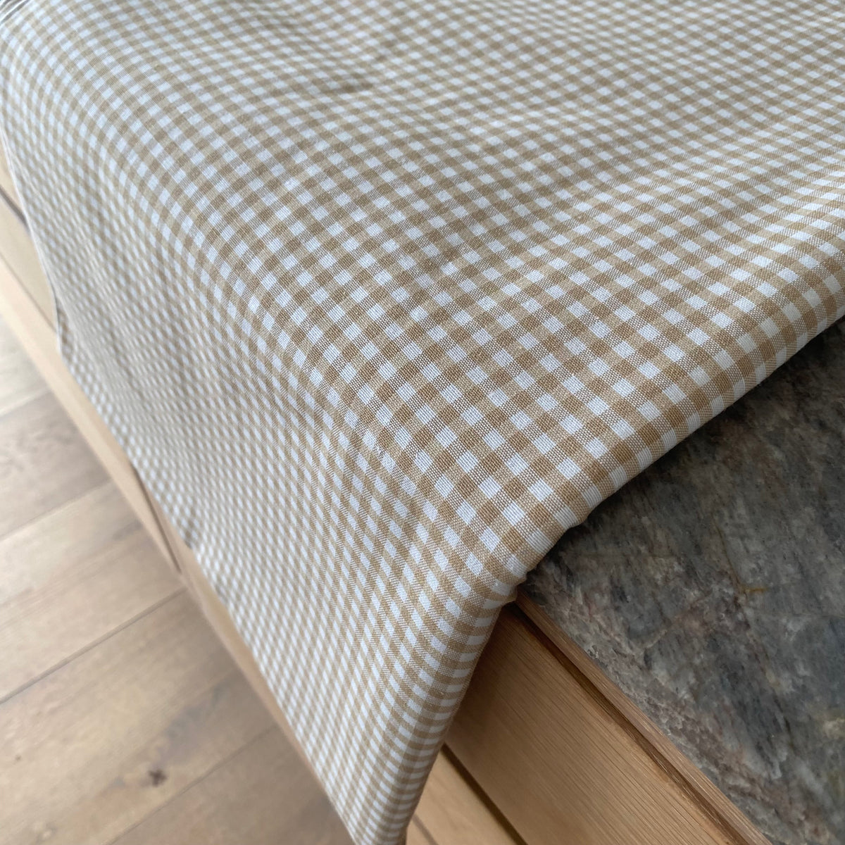 Vichy-dug med beige og hvide tern, foldet på et bord med stoffet hængende over kanten.