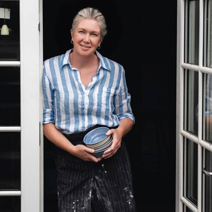 Dansk keramiker Rikke Mangelsen foran sit keramikværksted med håndlavede keramikskåle i hånden.