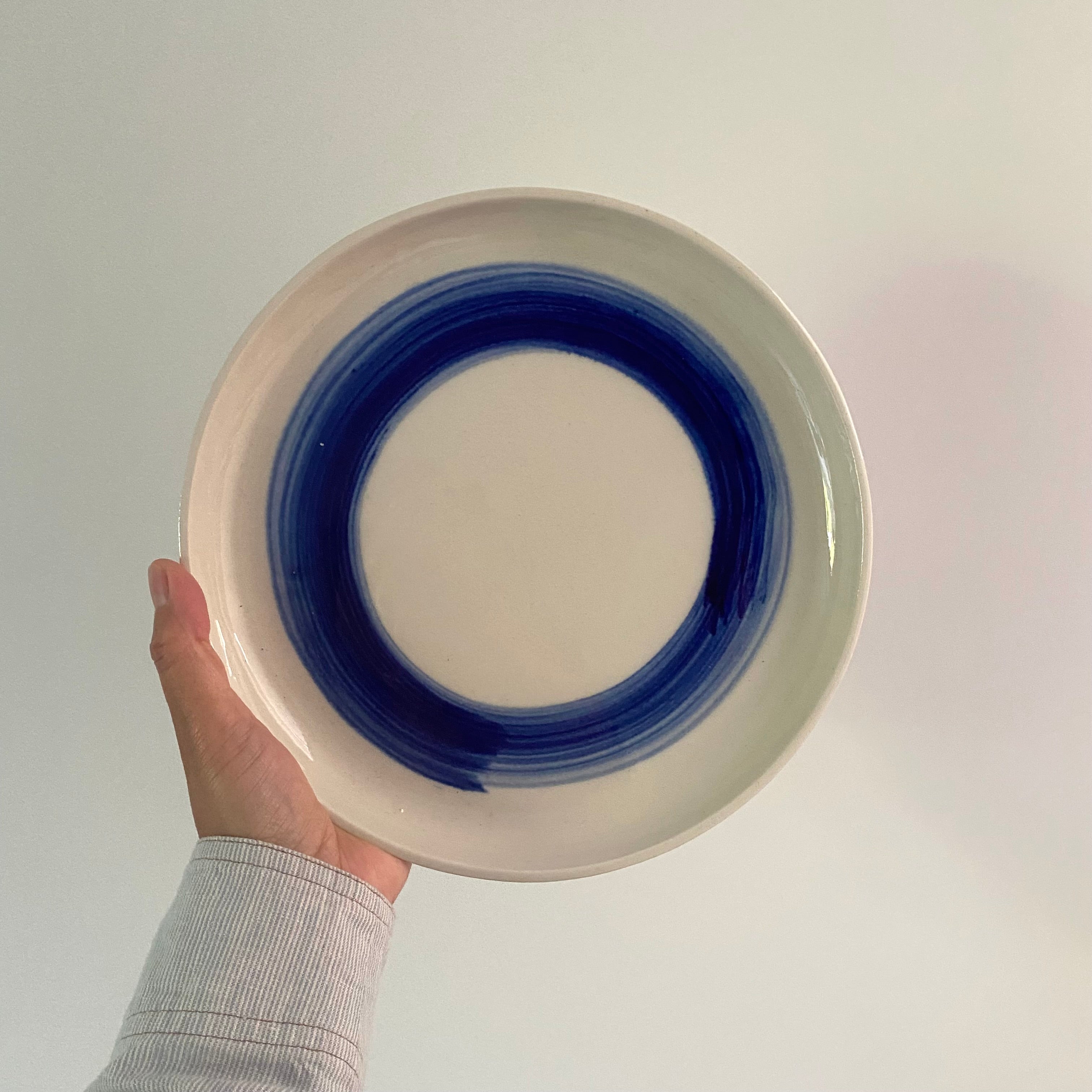 Håndlavet tallerken med blå cirkel – keramik fra Bornholm, holdt i hånden