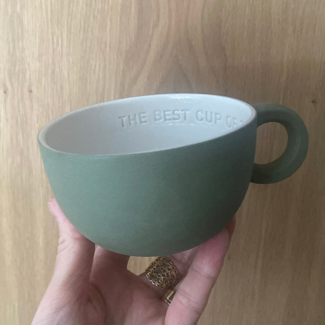 Chubby tekop i olivengrøn håndlavet keramik holdt i hånden med teksten “The best cup of tea is with you” indeni