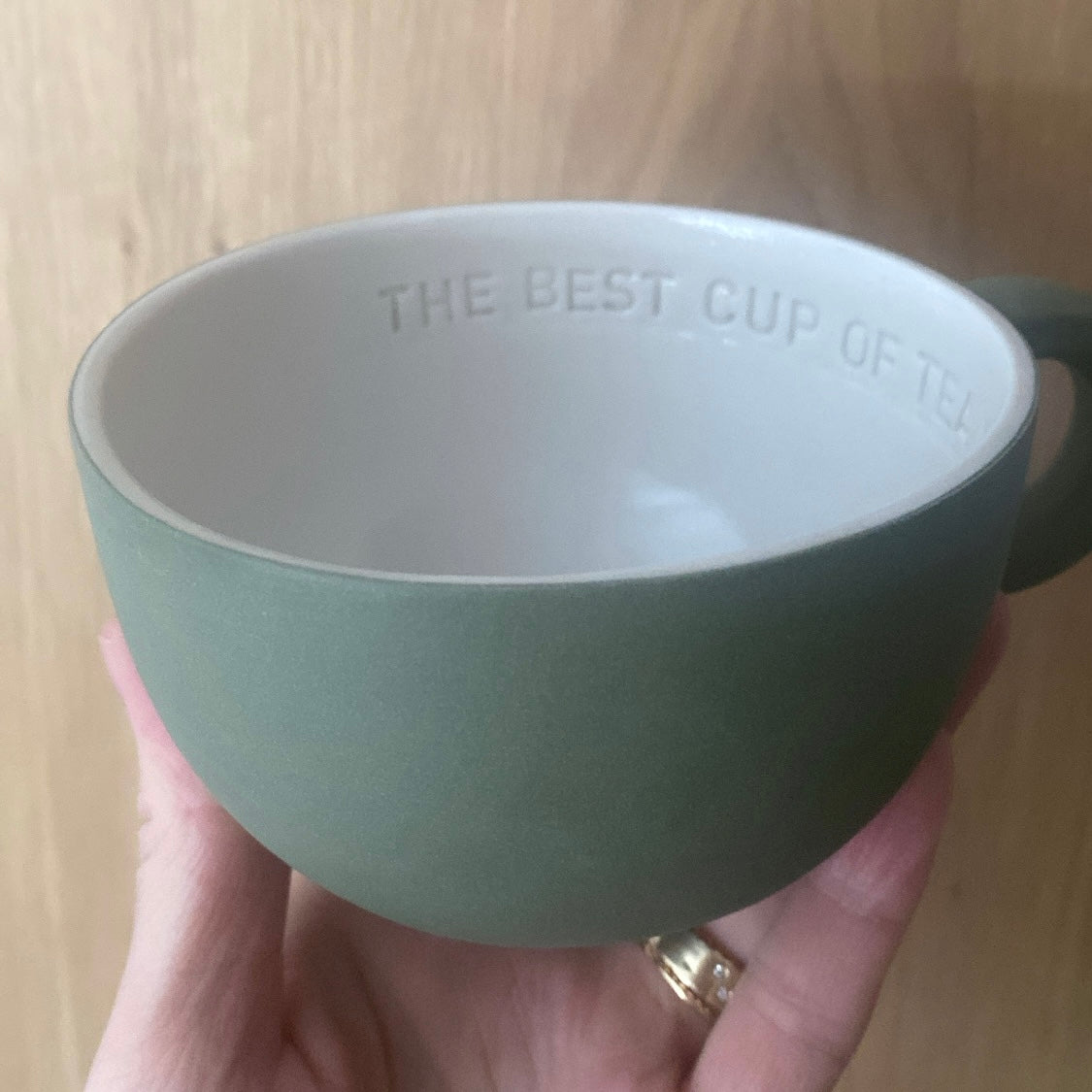 Chubby tekop i olivengrøn håndlavet keramik holdt i hånden med teksten “The best cup of tea is with you” indeni