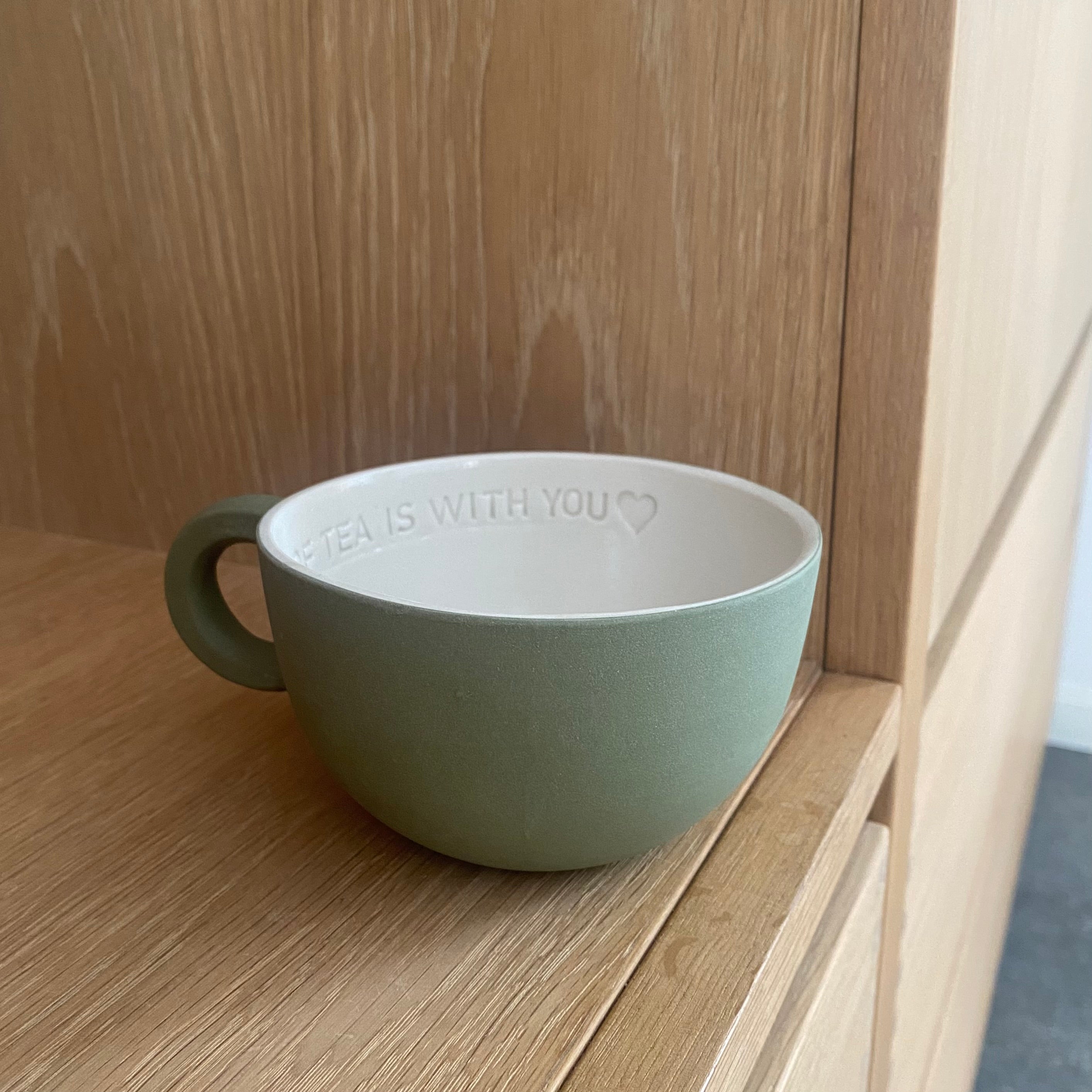 Chubby tekop med hank i olivengrøn håndlavet keramik med hvid glasur og teksten “The best cup of tea is with you”