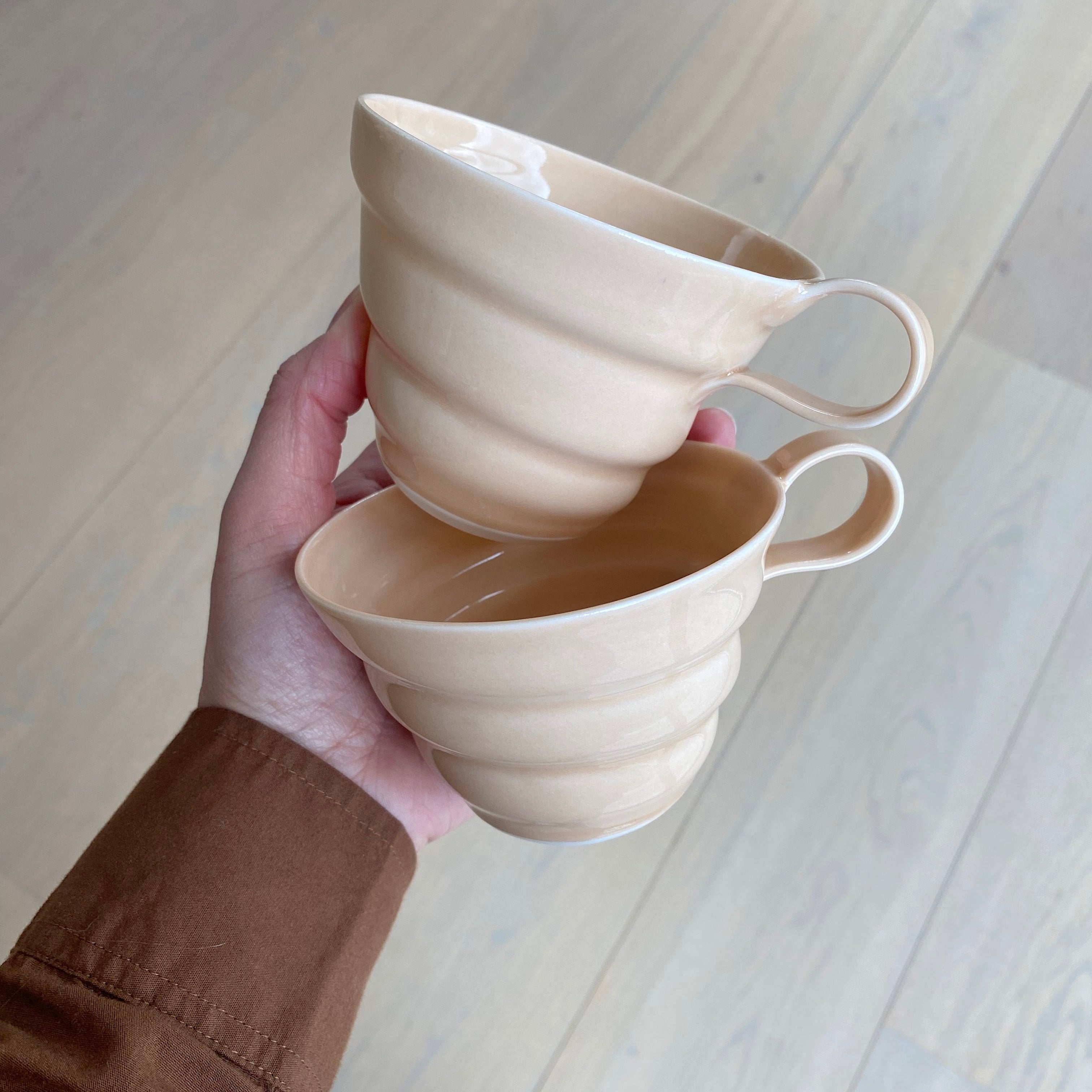 To hånddrejede kaffekopper med hank af keramiker Rikke Mangelsen. Begge kopper er i porcelæn og farven melon