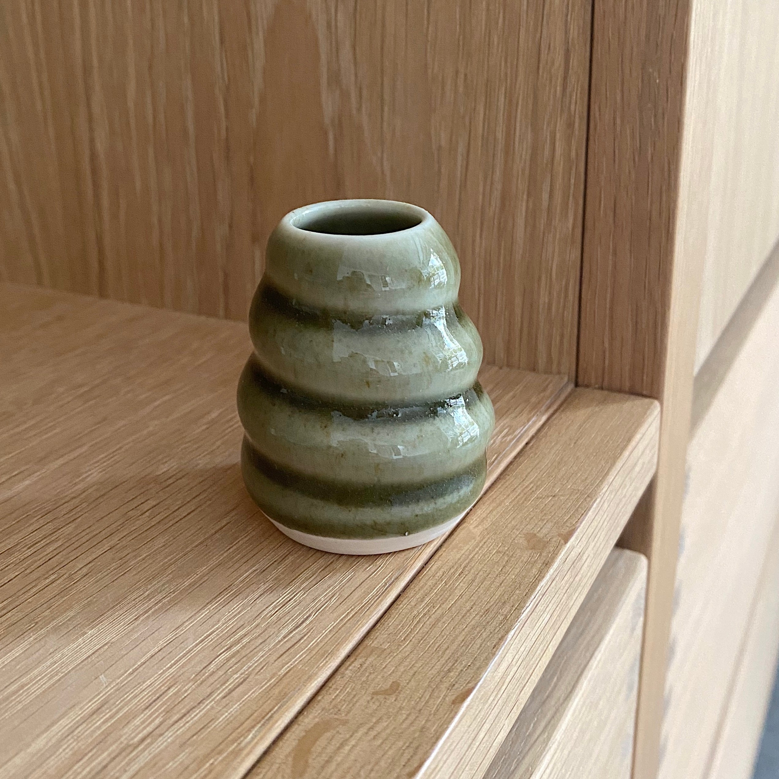 lille haanddrejet keramikvase i mosgroen til små stilke fra haven. vasen har et snoet spiraldesign og er i smuk groen glasur