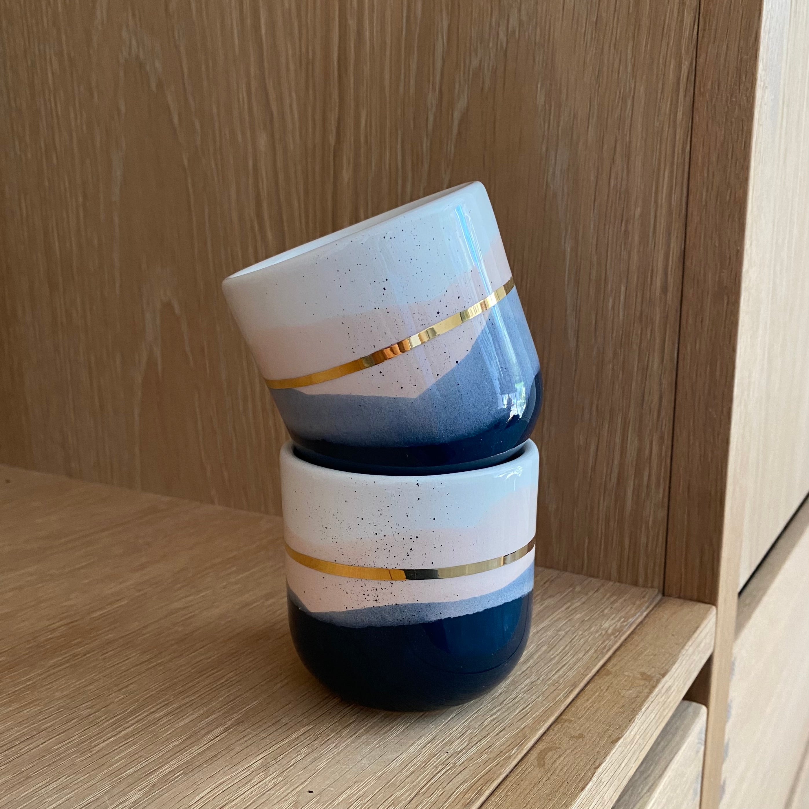 To håndlavede cappuccinokopper stablet oveni hinanden fra Marinski. Koppen hedder landscape i blå og creme med guldstreg