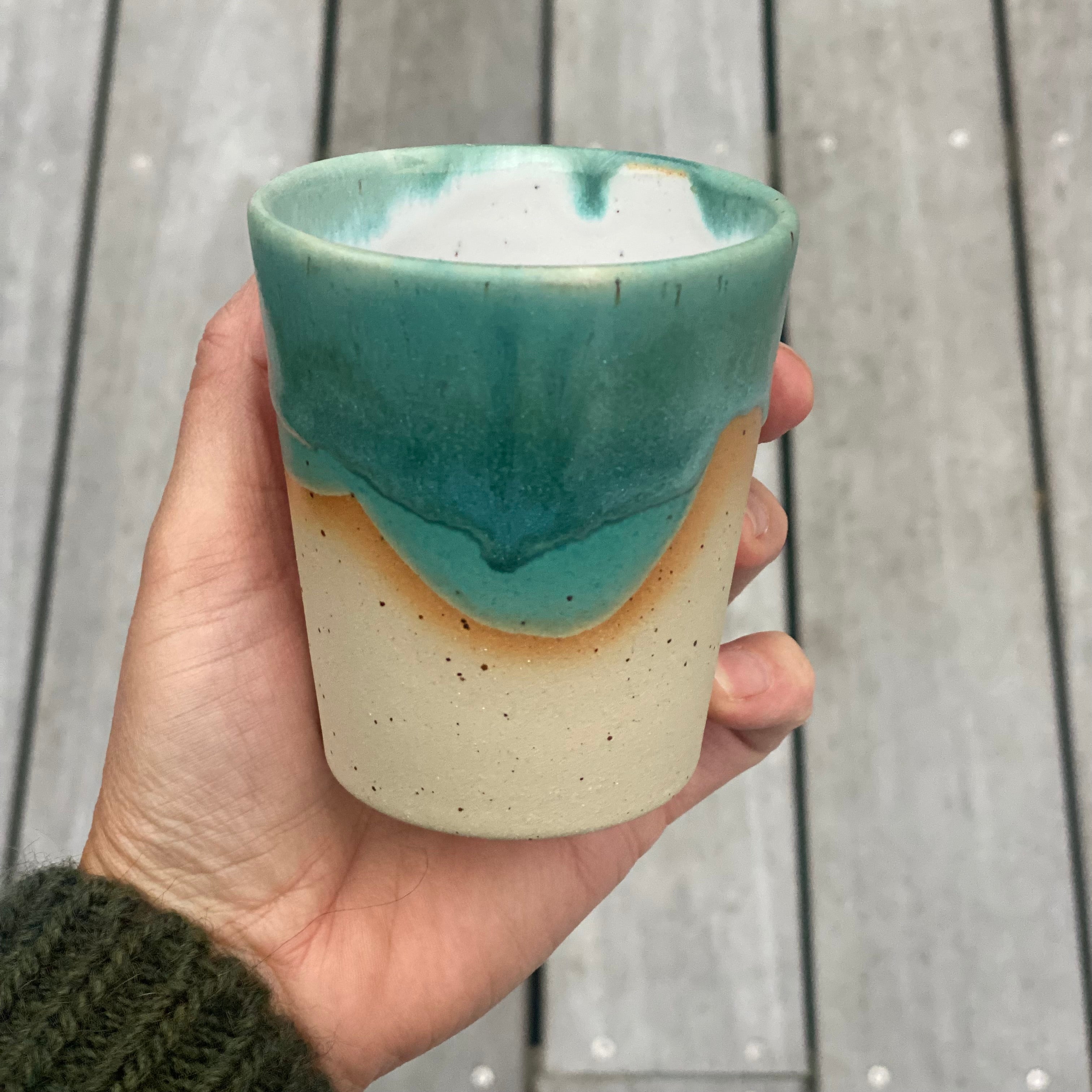 Hånddrejet flat white kop fra Marinski Heartmades i grøn glasur og naturfarvet stentøj – holdes i hånden