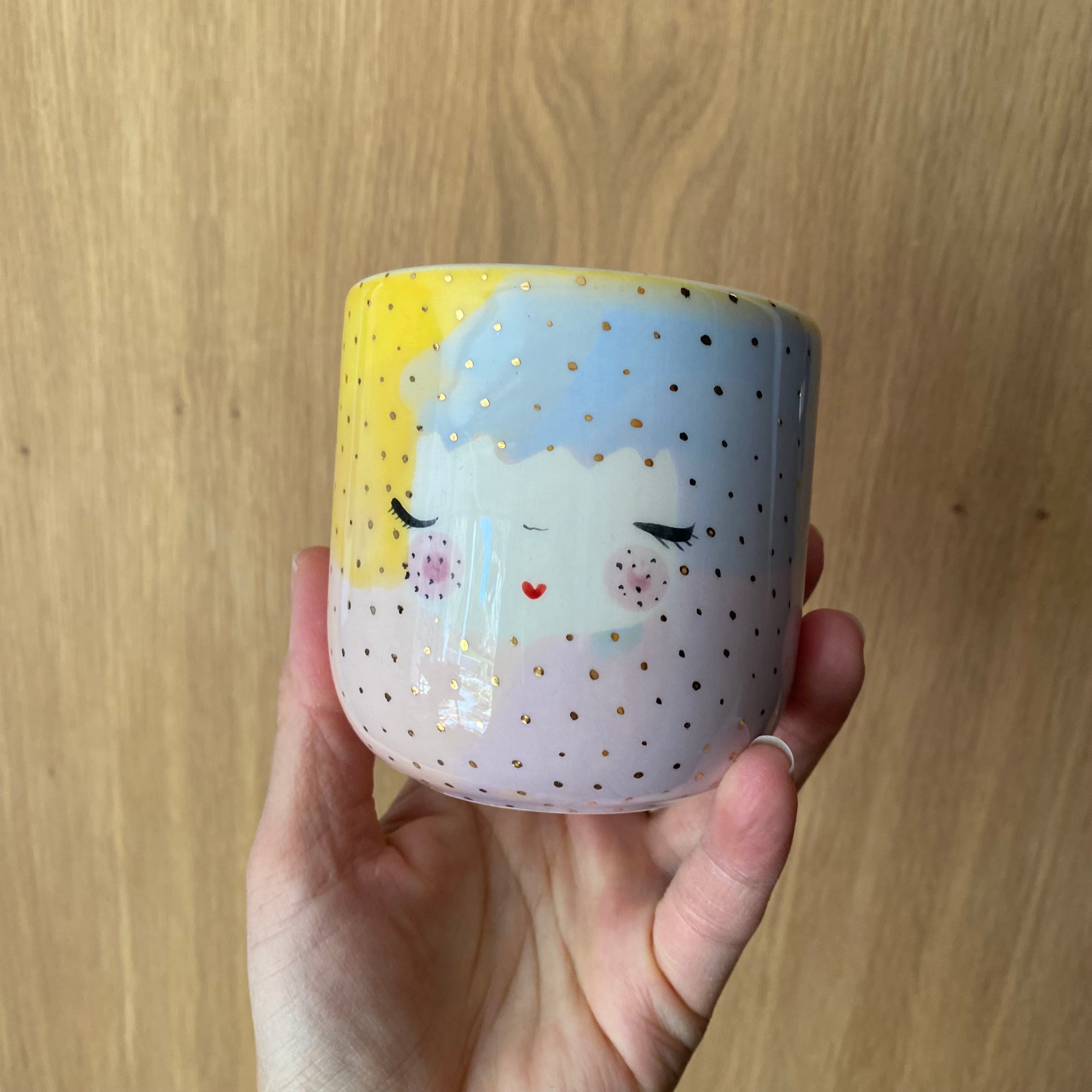 Håndlavet kaffekop Dots Unicorn med pastelfarver, ansigt og guldprikker fra Marinski Heartmades, holdt i hånden