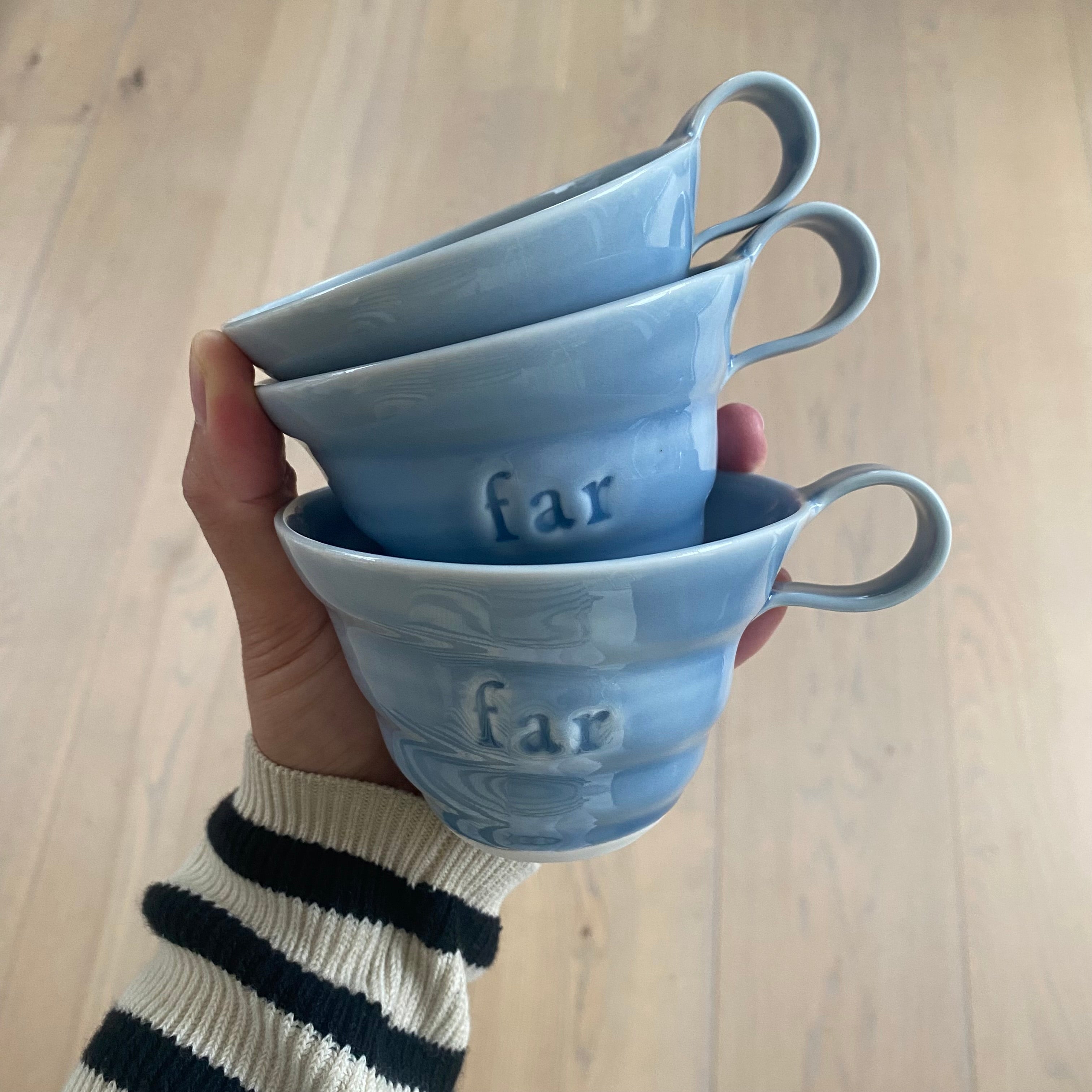 Navnekop til far i lyseblå porcelæn – tre far kopper holdt i hånden med teksten Far i glasuren, håndlavet af Rikke Mangelsen