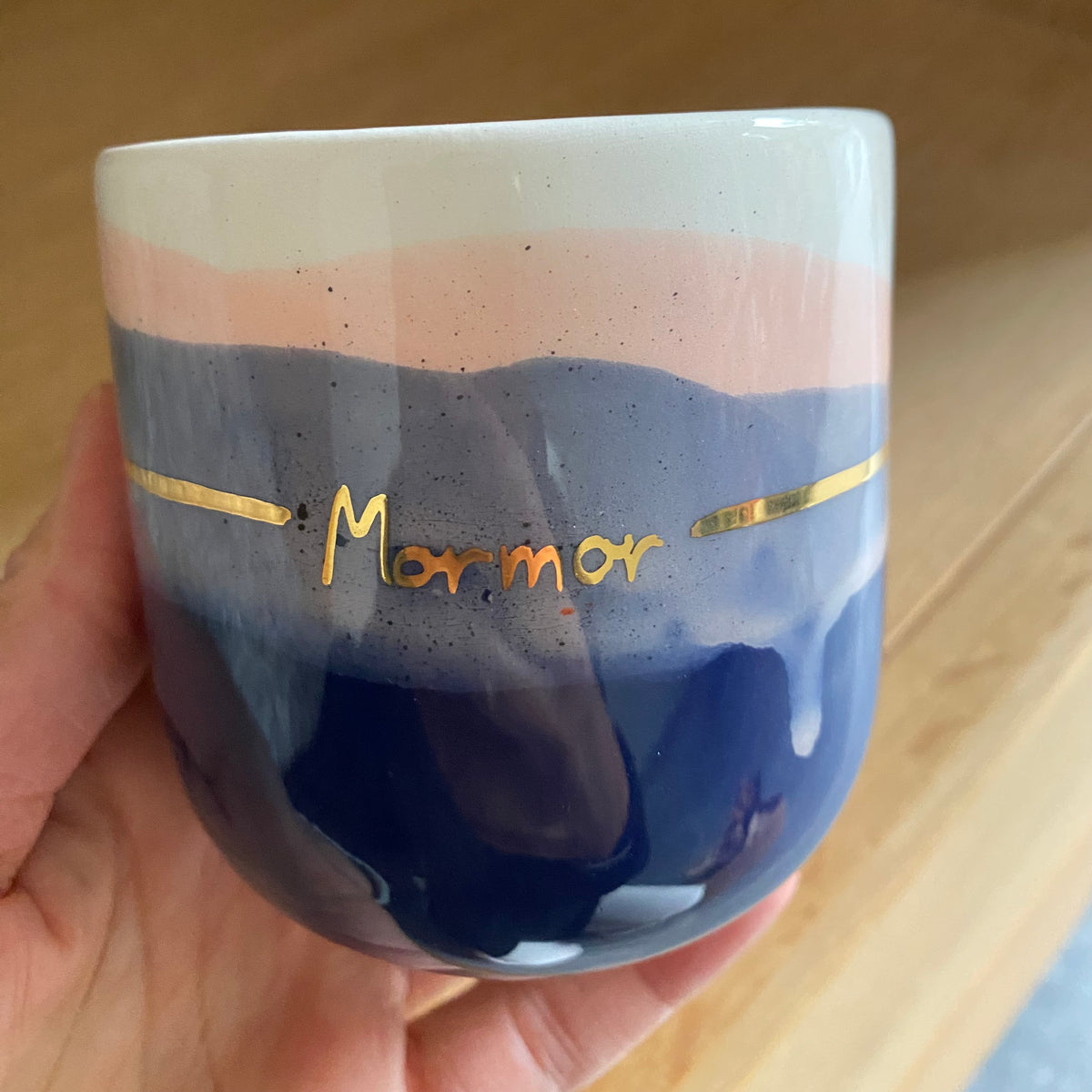 Kop med tekst – nærbillede af Mormor skrevet i guld på en blå og blush keramikkop holdt i hånden.