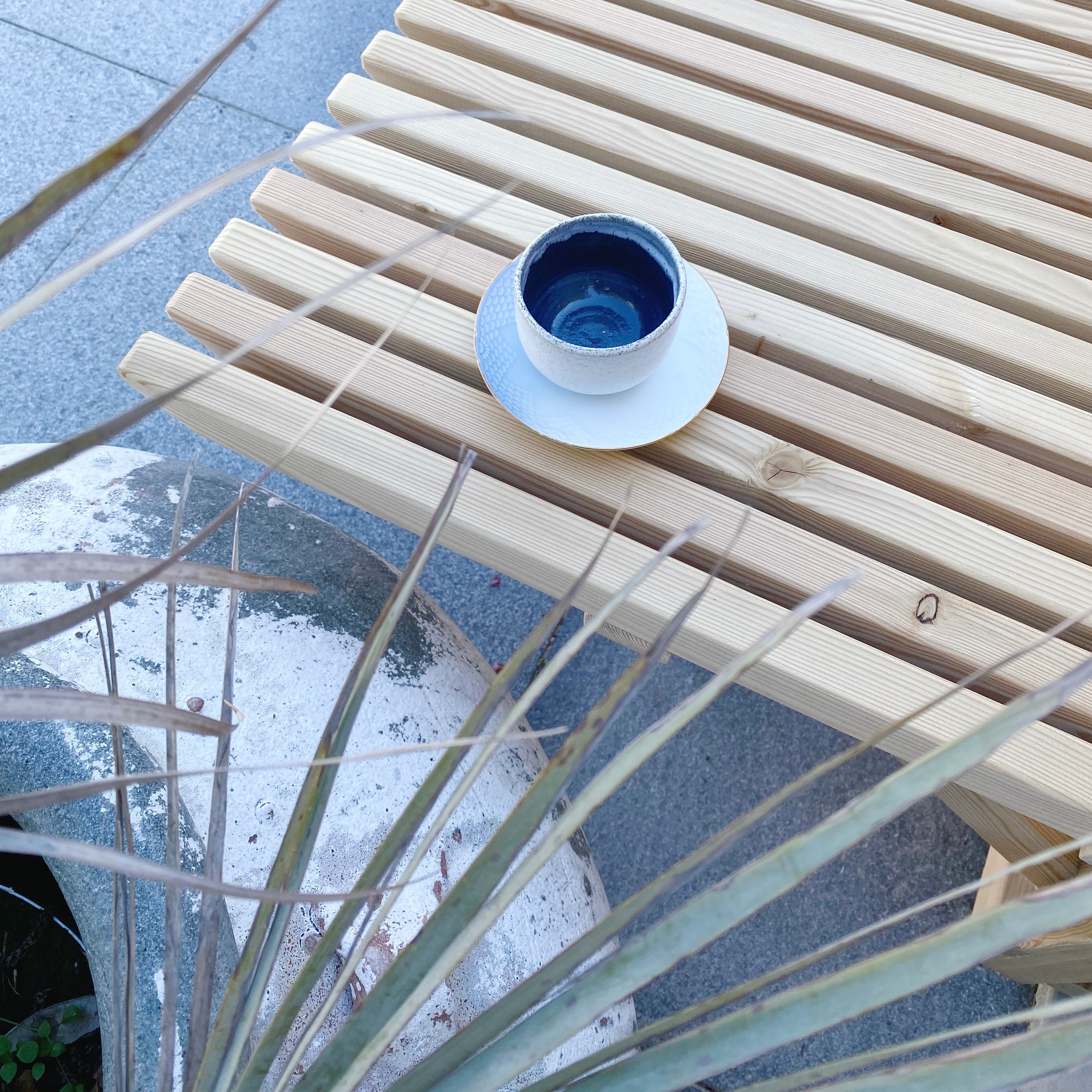 Hånddrejet espressokop i mørkeblå keramik på havebænk med plante – dansk keramik af Tasja P