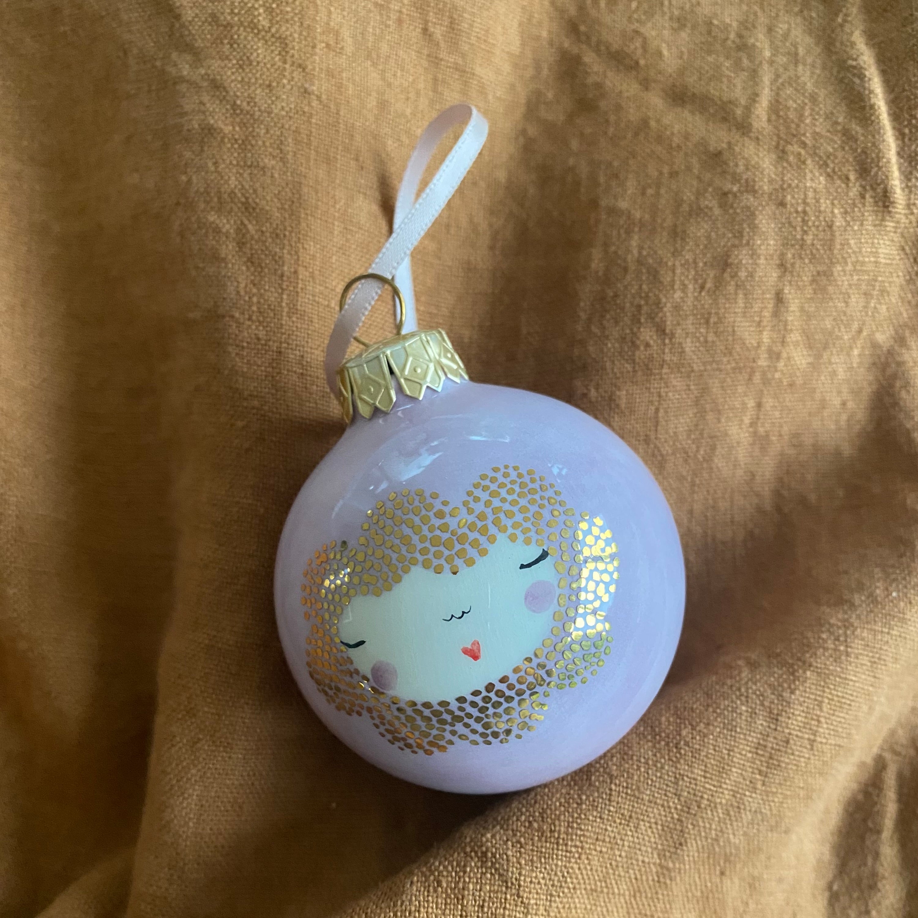 Julekugle i lyselilla med gulddetaljer og håndtegnet ansigt – hænger på et grantræ