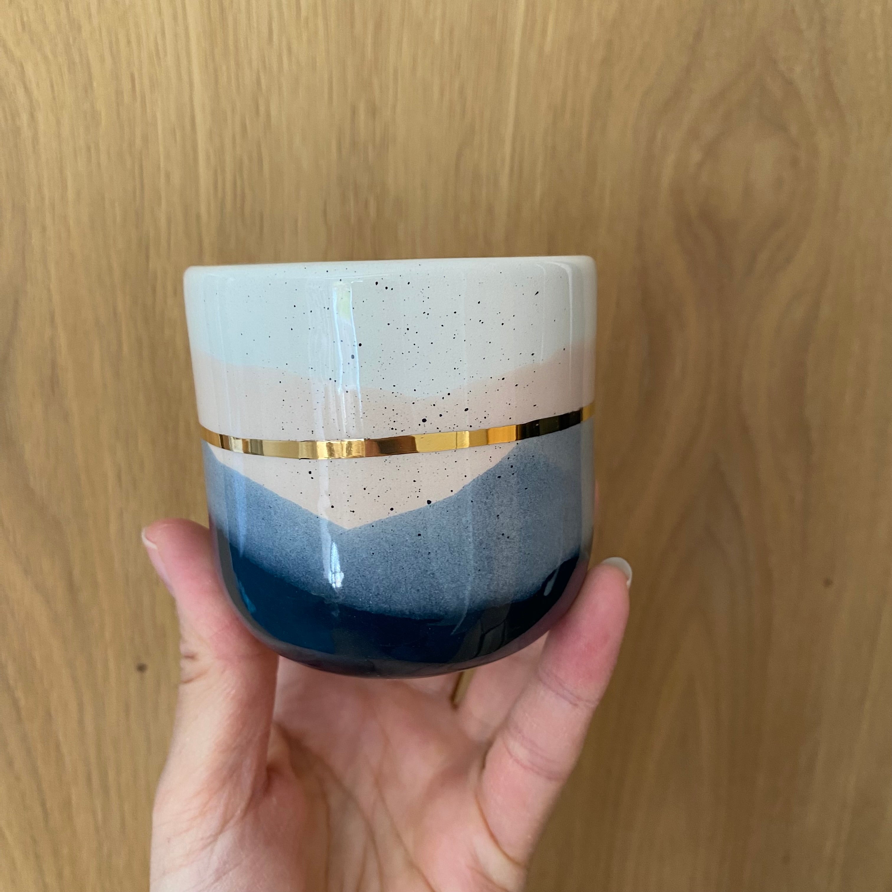 Håndlavet cappuccinokop holdt i hånden fra Marinski - landscape kop i blå og creme med guldbånd