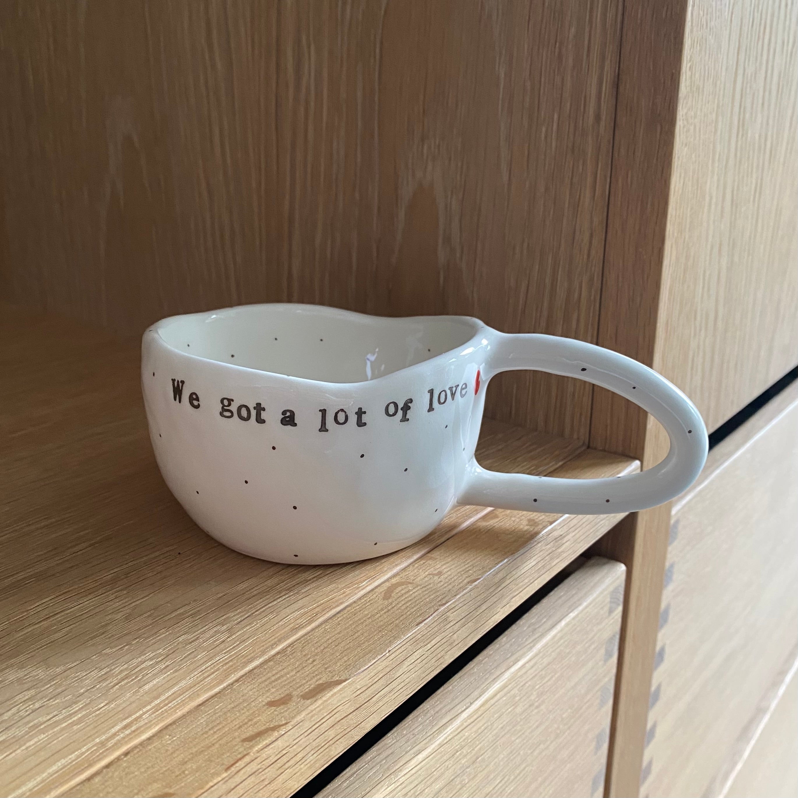 Håndlavet kop med hank og tekst “We got a lot of love” i hvid keramik med sorte prikker