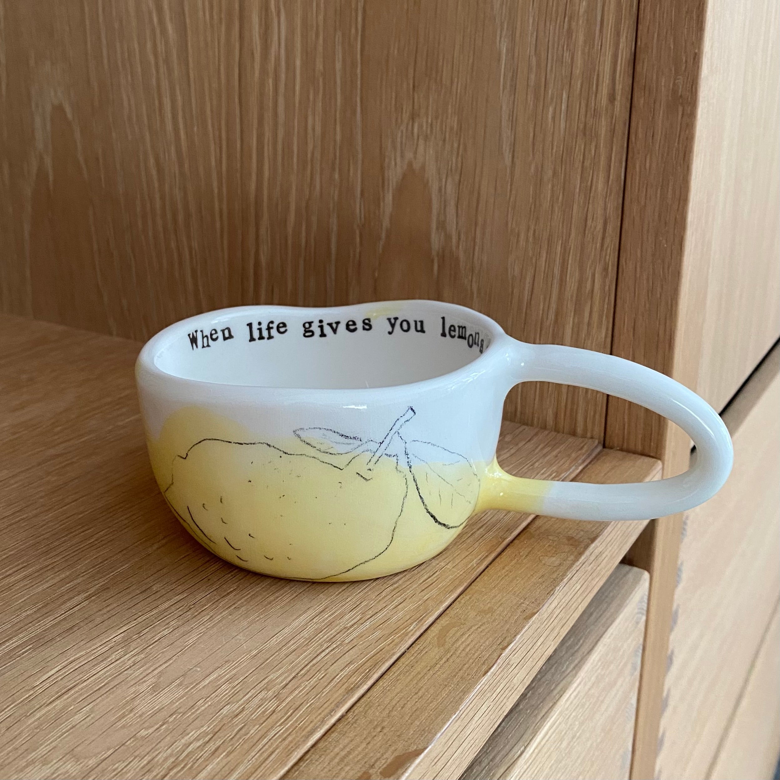 Håndlavet kop med hank og teksten “When life gives you lemons” i hvid keramik og håndtegnede citron udenpå