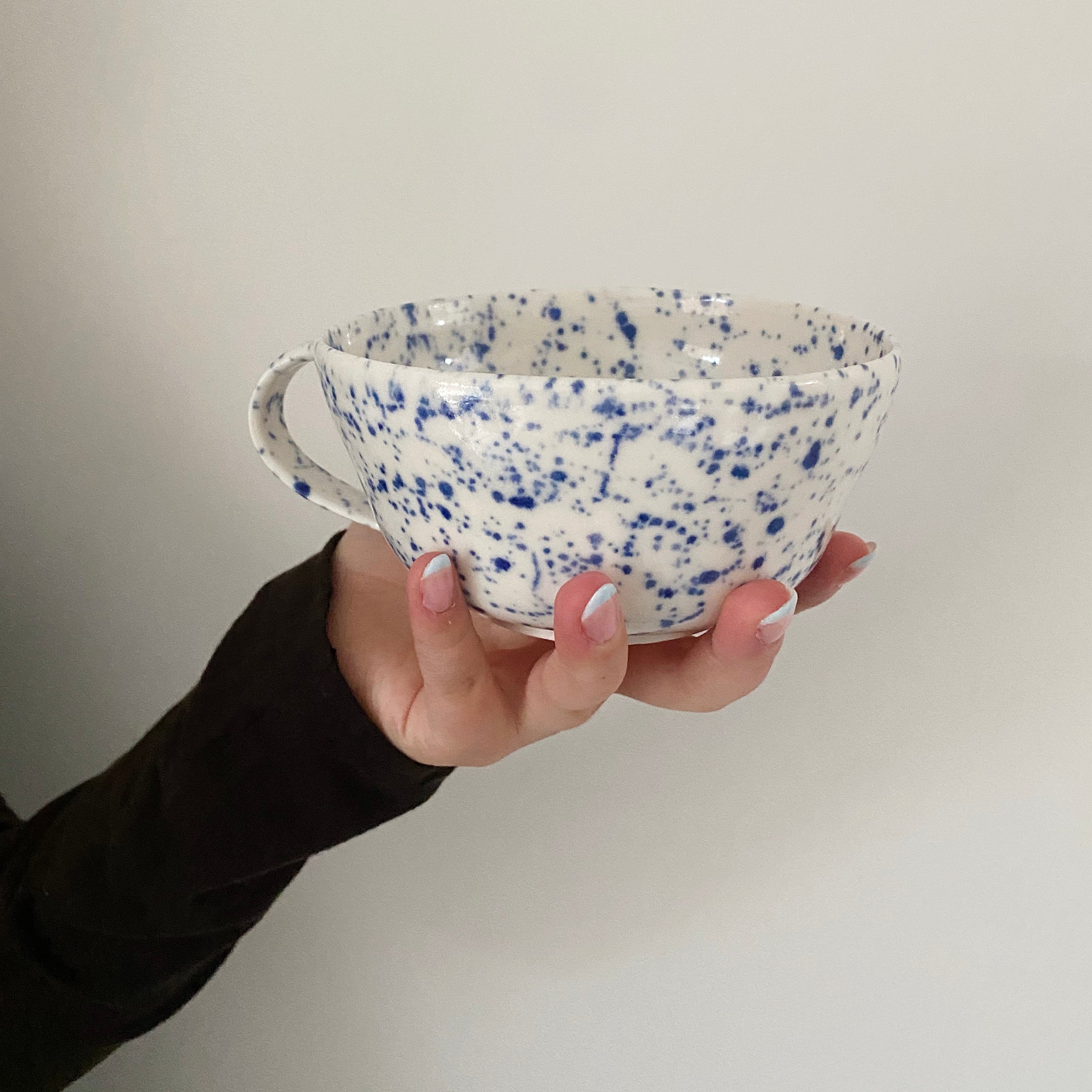 Håndlavet tekop i porcelæn med blå splash, holdt i hånden